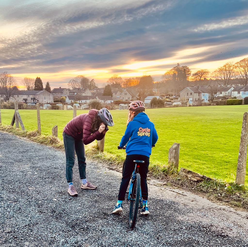 Woman in a pink jacket taking a photo of a girl on a bike in a blue hoodie
