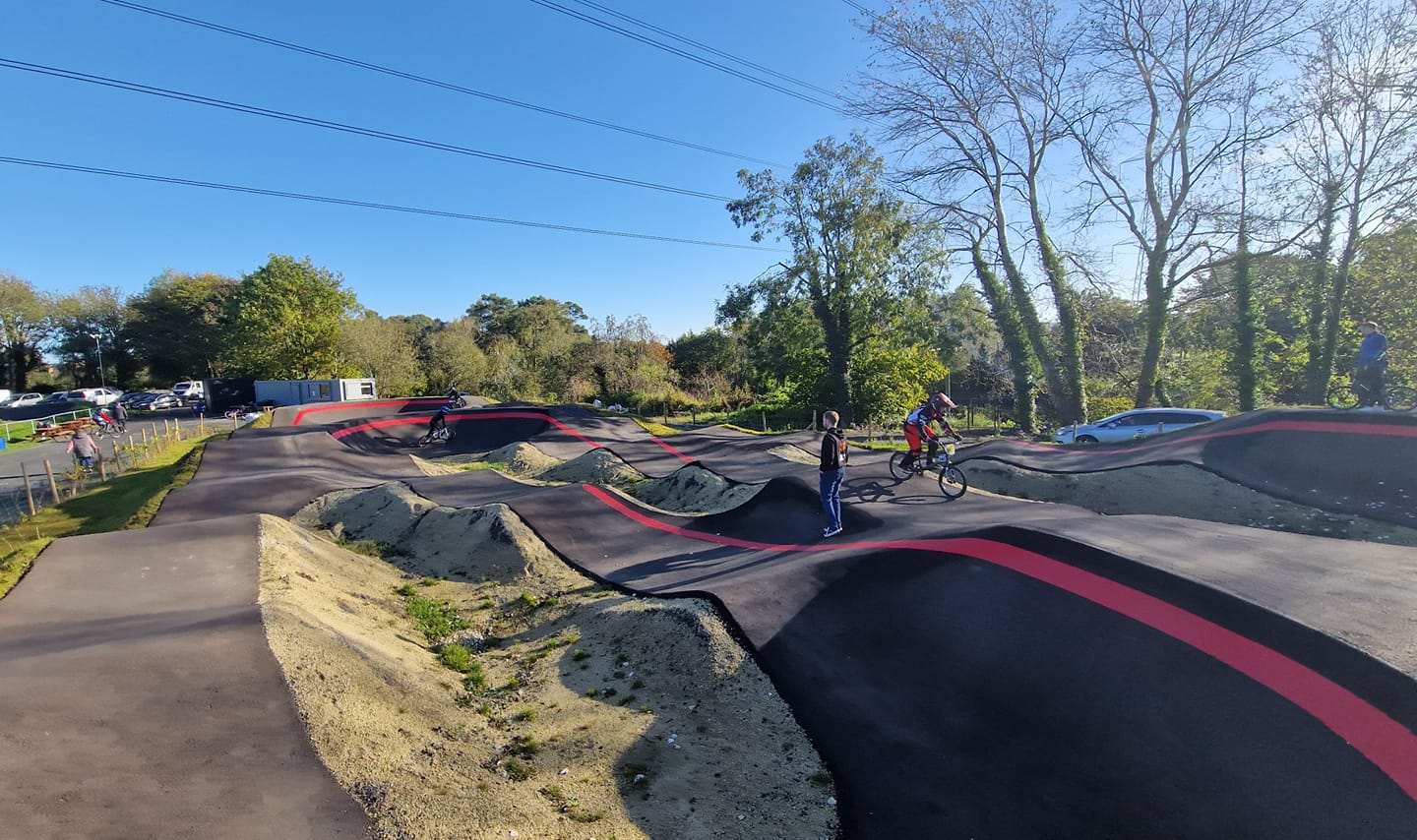 gray and red pump track with lots of BMX riders