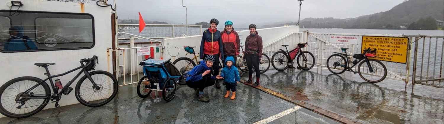 A group of adults with a small child, all dressed in waterproofs, waiting with their bikes and a trailer at a ferry port
