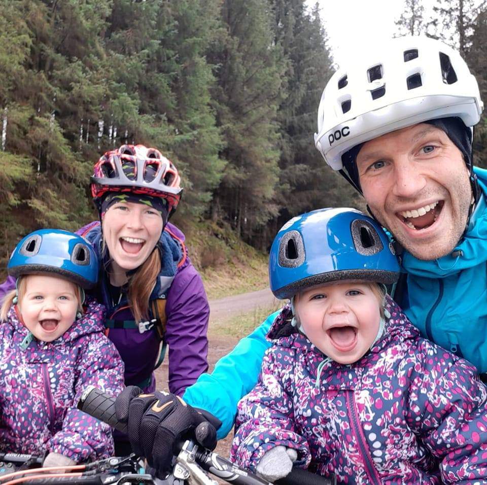 Two parents and their twin daughters smiling at the camera in their bike helmets and waterproofs