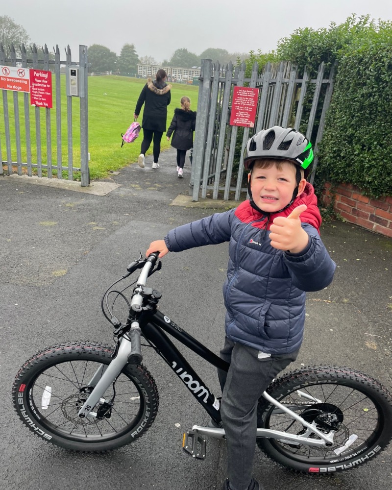 cycling to school- a boy outside school with his thumbs up.