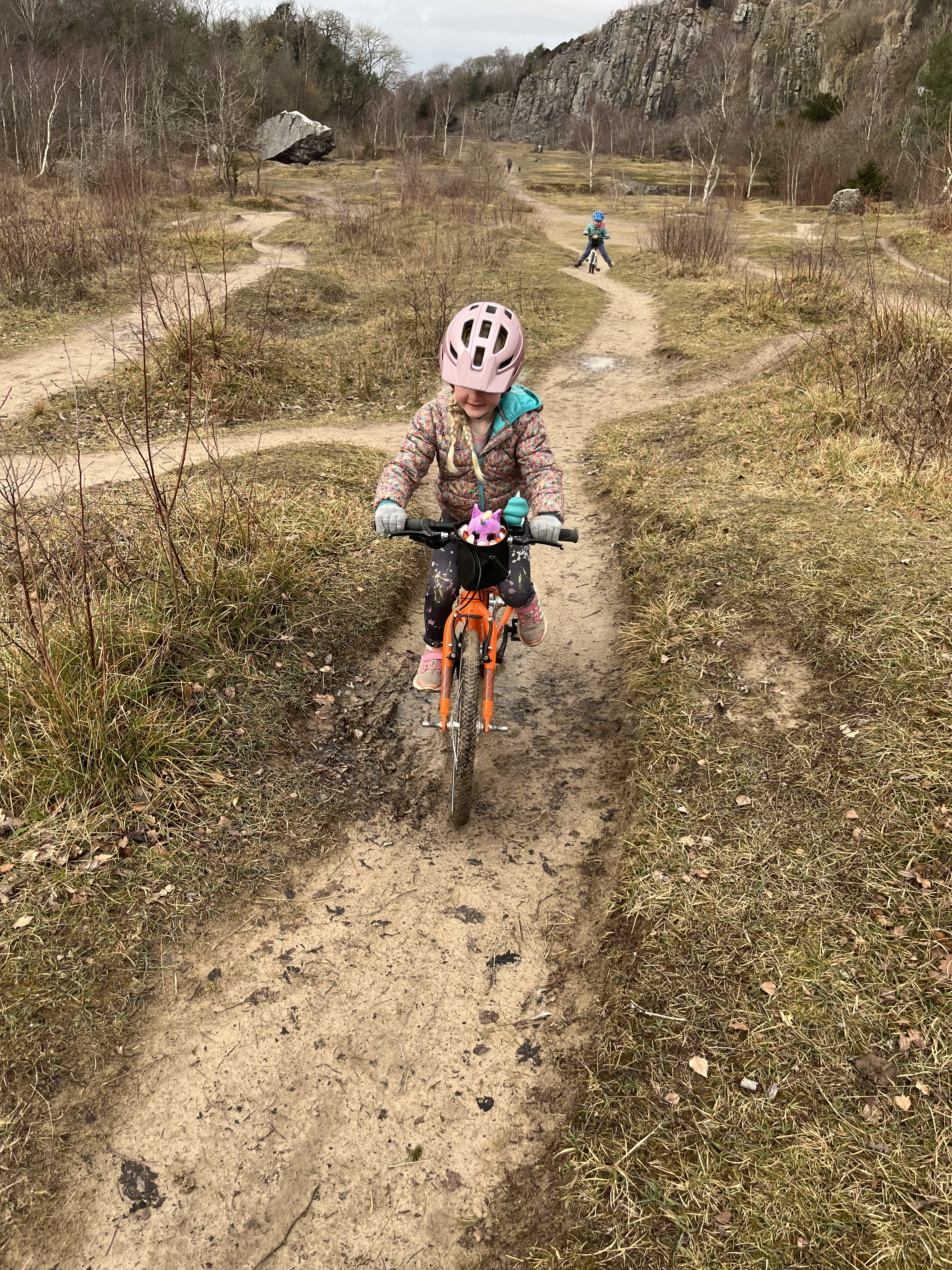 Yomo 20 kids bike being ridden along a pump dirt track by a young girl in a pink helmet
