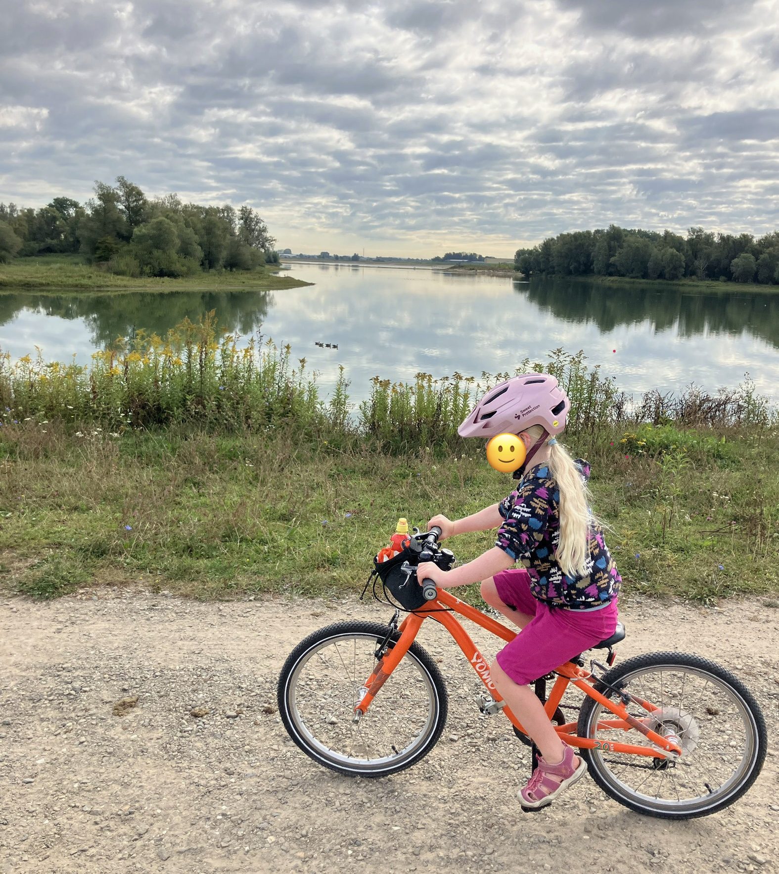 YOMO 20 kids bike being ridden by a young girl along a dirt path beside a lake