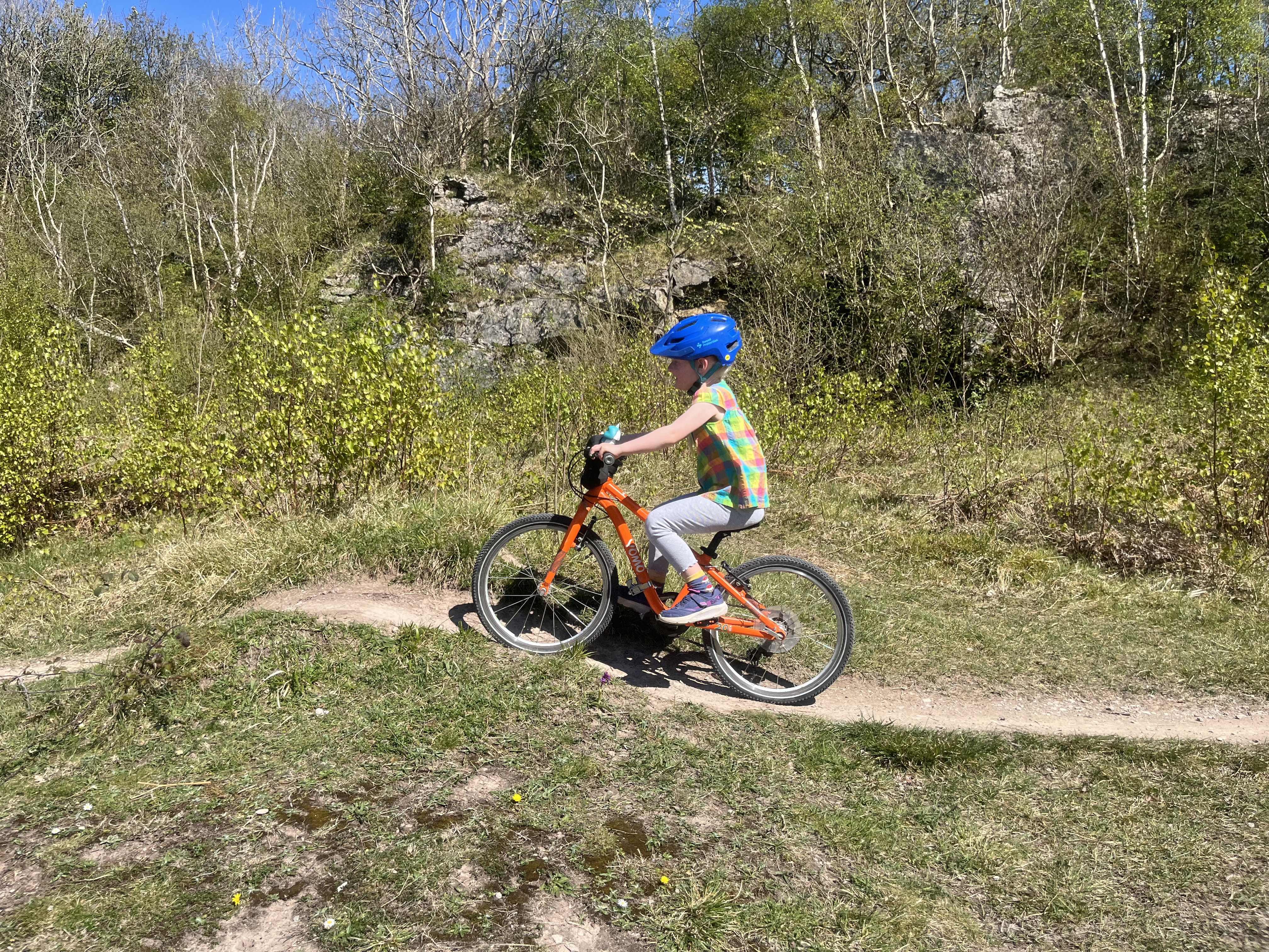 Young girl riding the Yomo 20 orange kids bike along a dirt path over some small hills