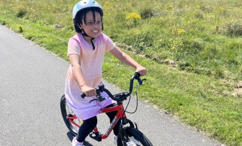 a girl in a pink dress riding her kidvelo rookie 18 bike