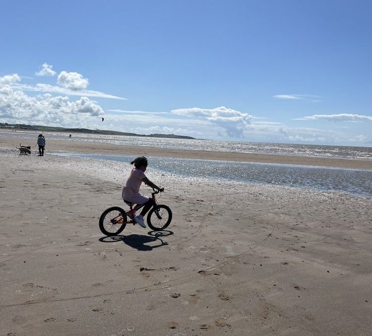 A young girl riding her Kidvelo rookie 18 bike on the beach on a sunny day
