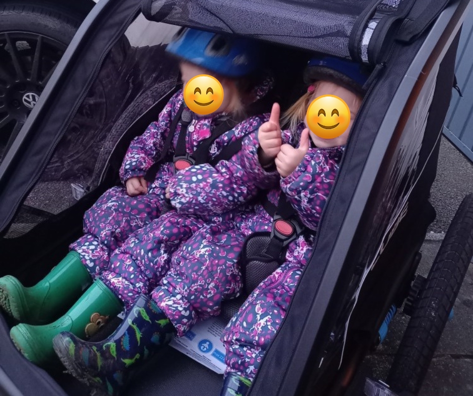Cube Kids Trailer Double CMPT review: Two twin girls smiling and doing a thumbs up in a bike trailer