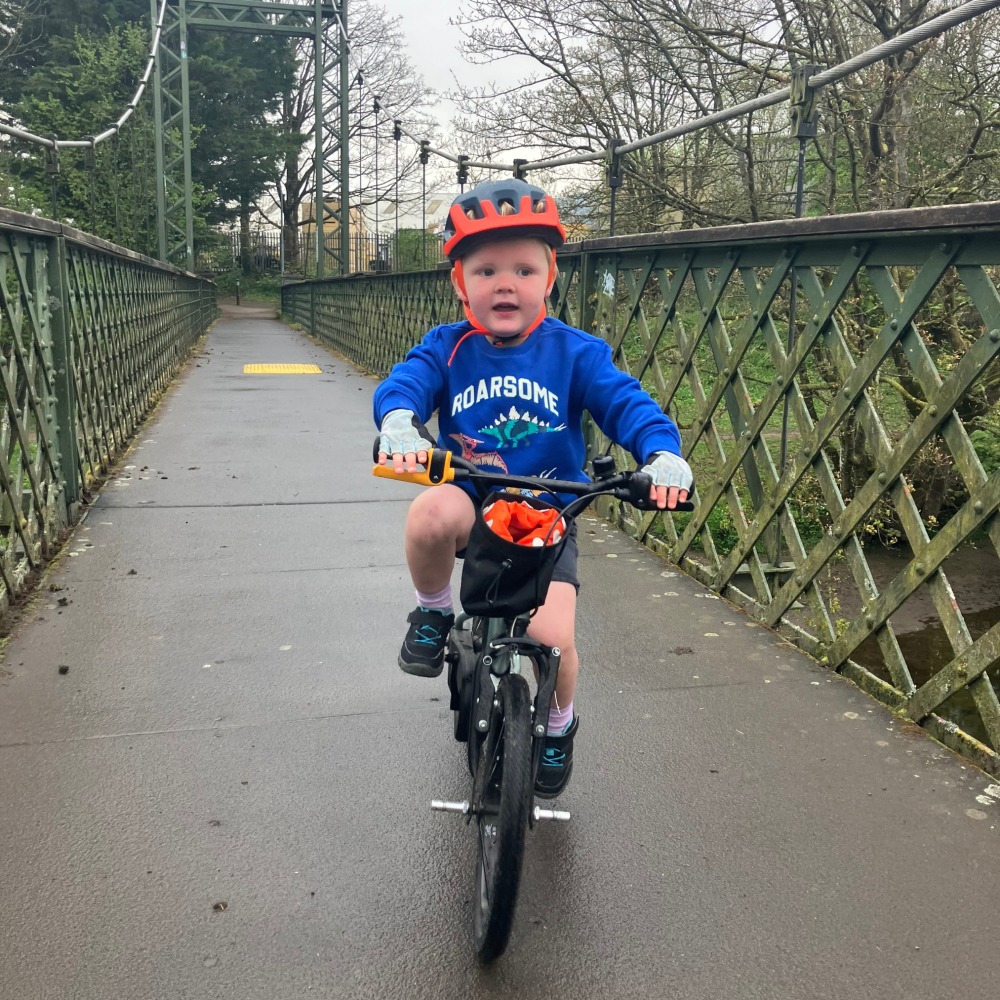 BTWIN 16 Discover 900 review- a smiling 3 year old boy in a 'roarsome' top riding across a bridge