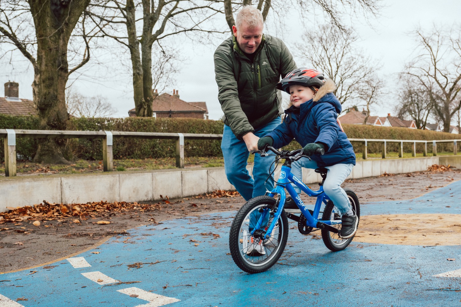 Adam LV Photography_ Shyre bikes Shoot-61 A little boy pedalling a blue Shyre bikes Hopton 16 in the park with his dad holding onto him and running alongside