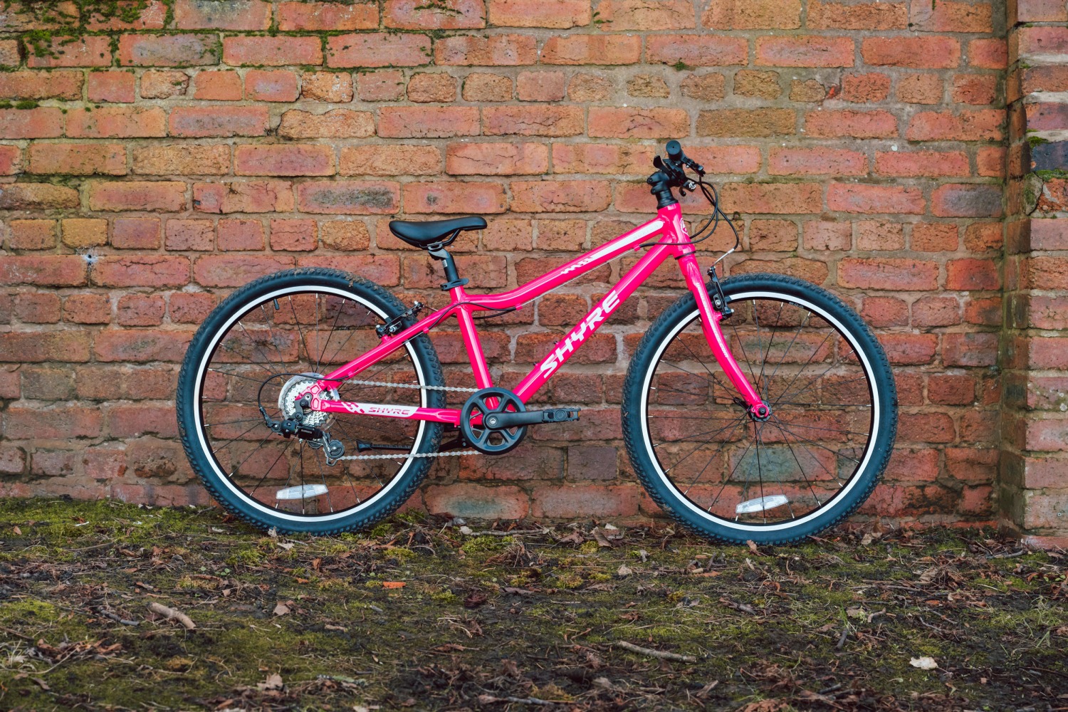 Adam LV Photography_ Shyre bikes Shoot static-2 A pink Shyre bikes Hopton 24 bike seen from the side, leaning against a brick wall
