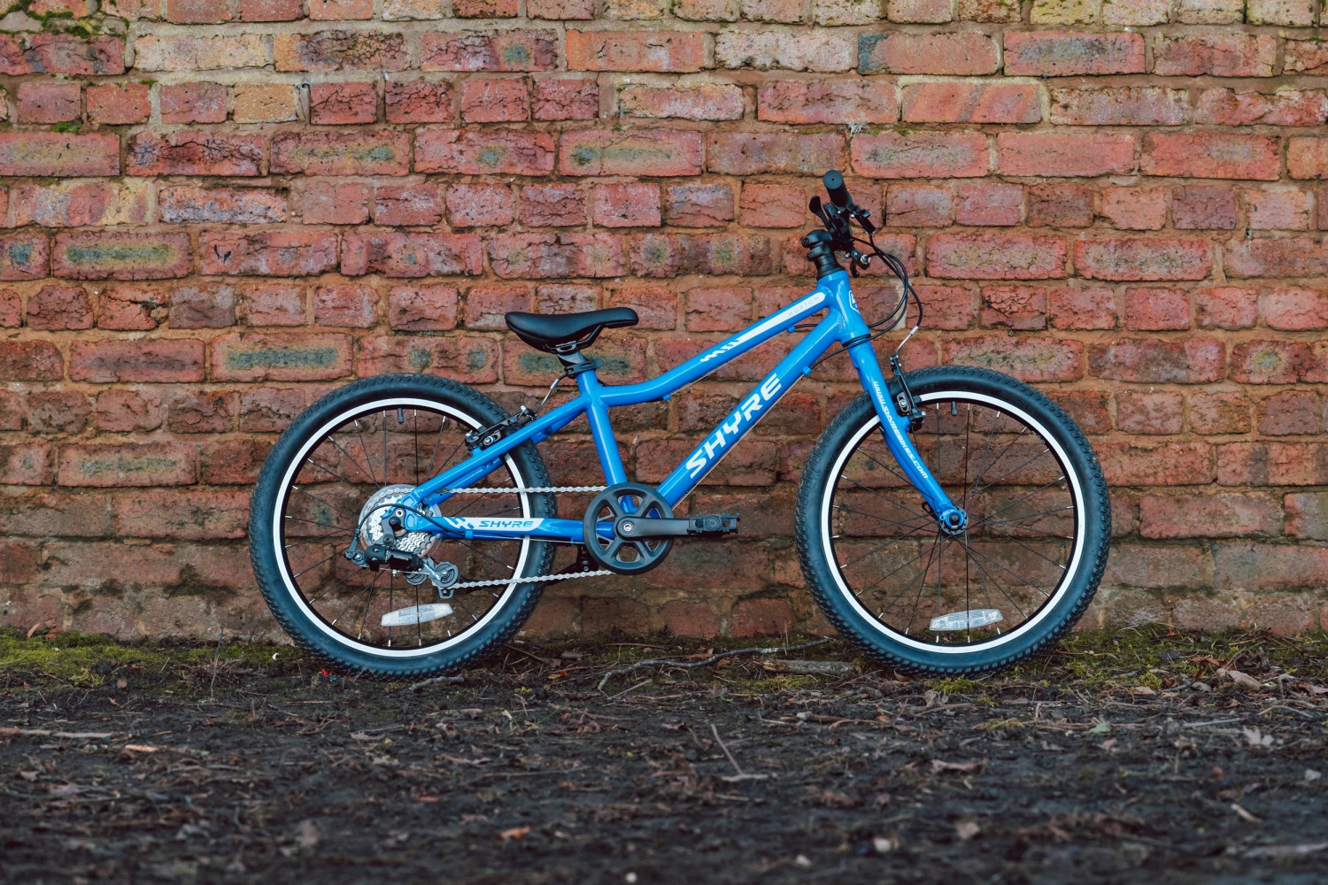 Adam LV Photography_ Shyre bikes Shoot static-48 A blue Shyre bikes Hopton 20 bike seen from the side, leaning against a brick wall