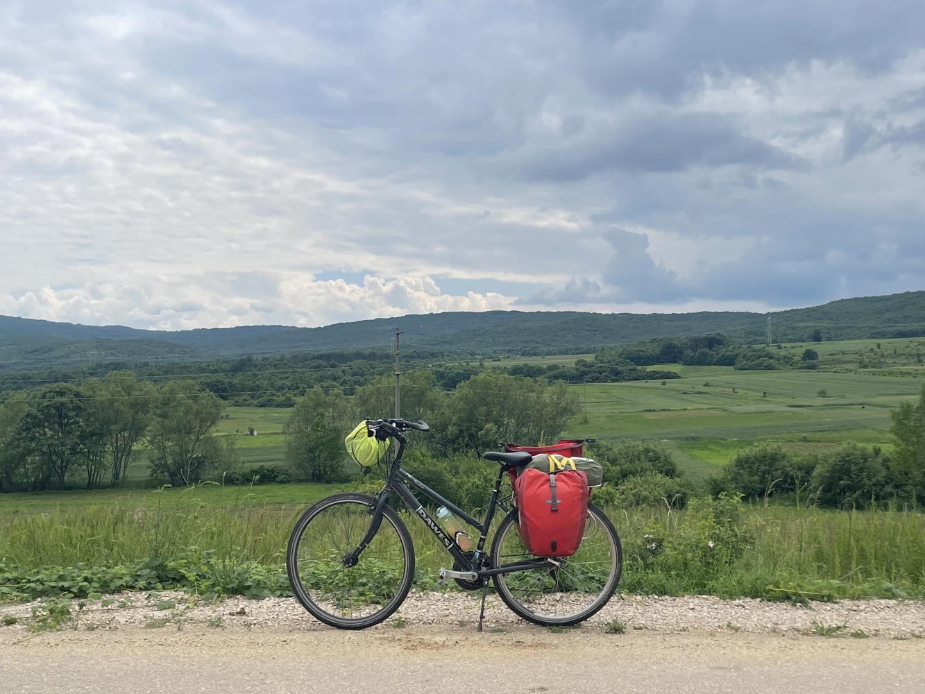 Sahir's cycle touring bike, loaded up with bags, propped up in front of a countryside landscape