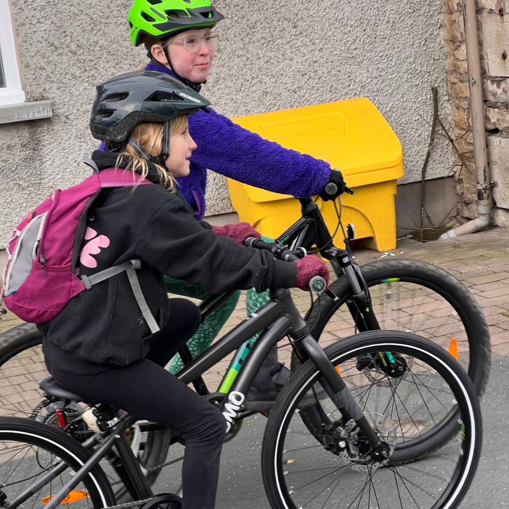 YOMO 24 review- a 7 year old girl wearing black with a pink backpack and gloves is riding to school with her sister