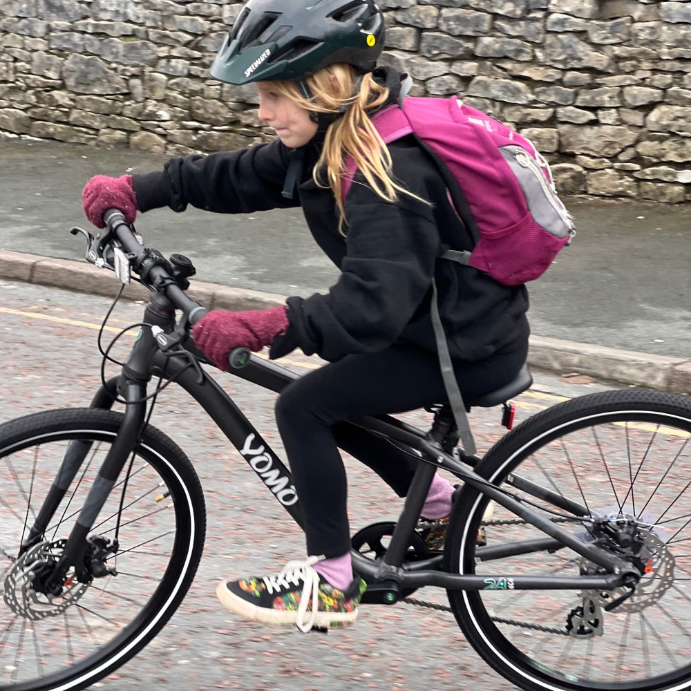 YOMO 24 review- a girl wearing black with a pink backpack and gloves is riding to school
