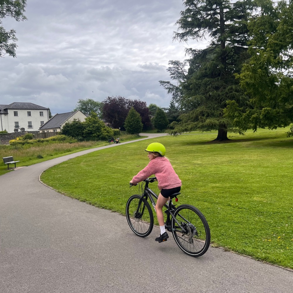 YOMO 24 review- a girl in a pink jumper and yellow helmet is riding around a park