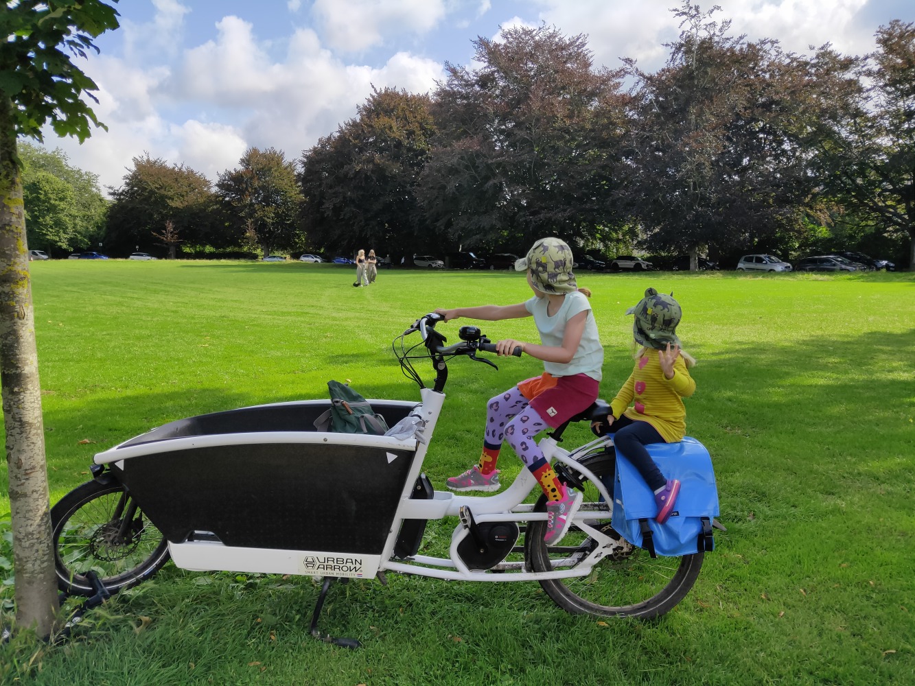 Two children sitting on a Urban Arrow Family cargo bike, looking away and waving