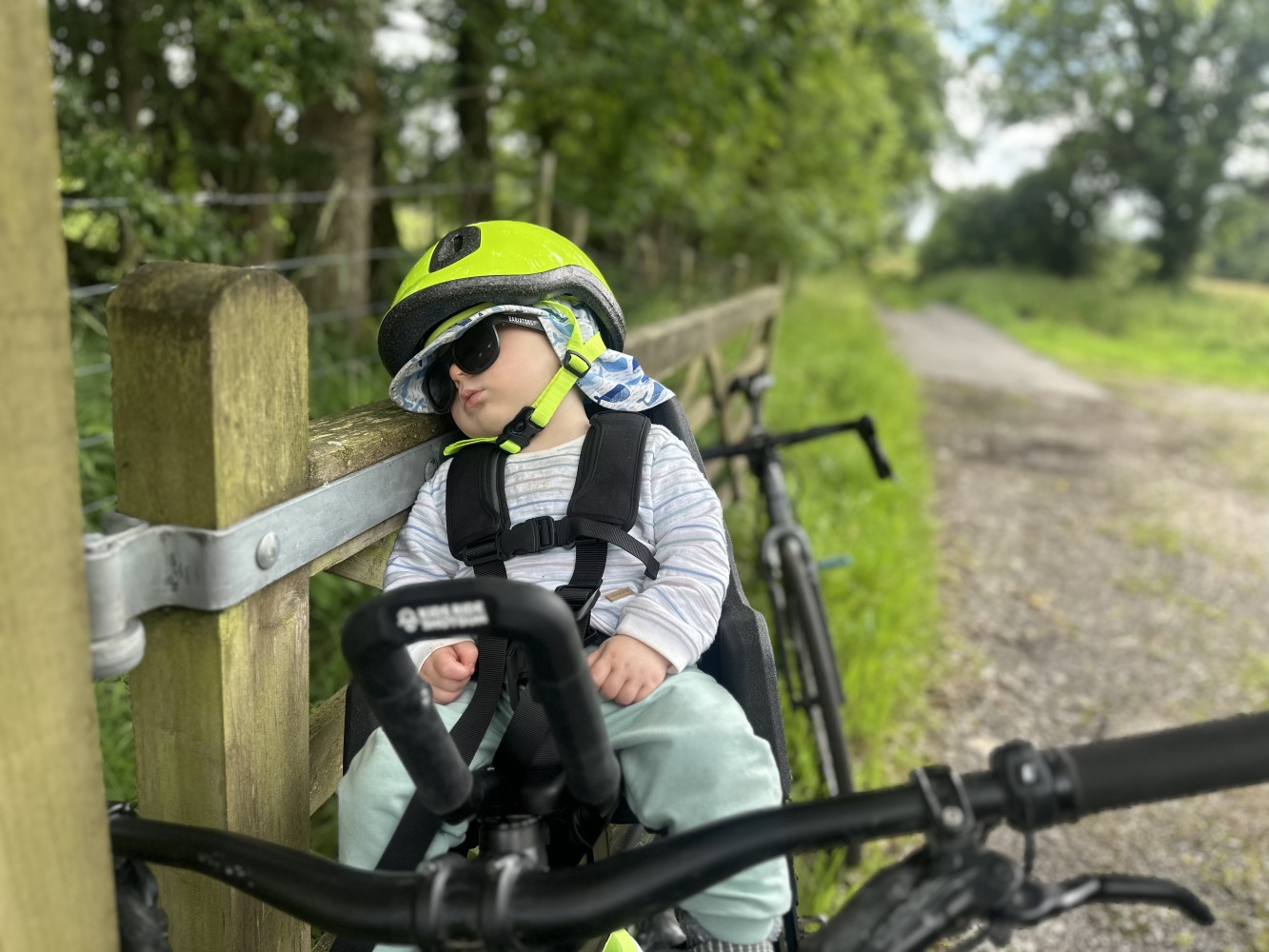 A little boy with a yellow helmet and sunglasses asleep on the kids ride shotgun pro evo seat