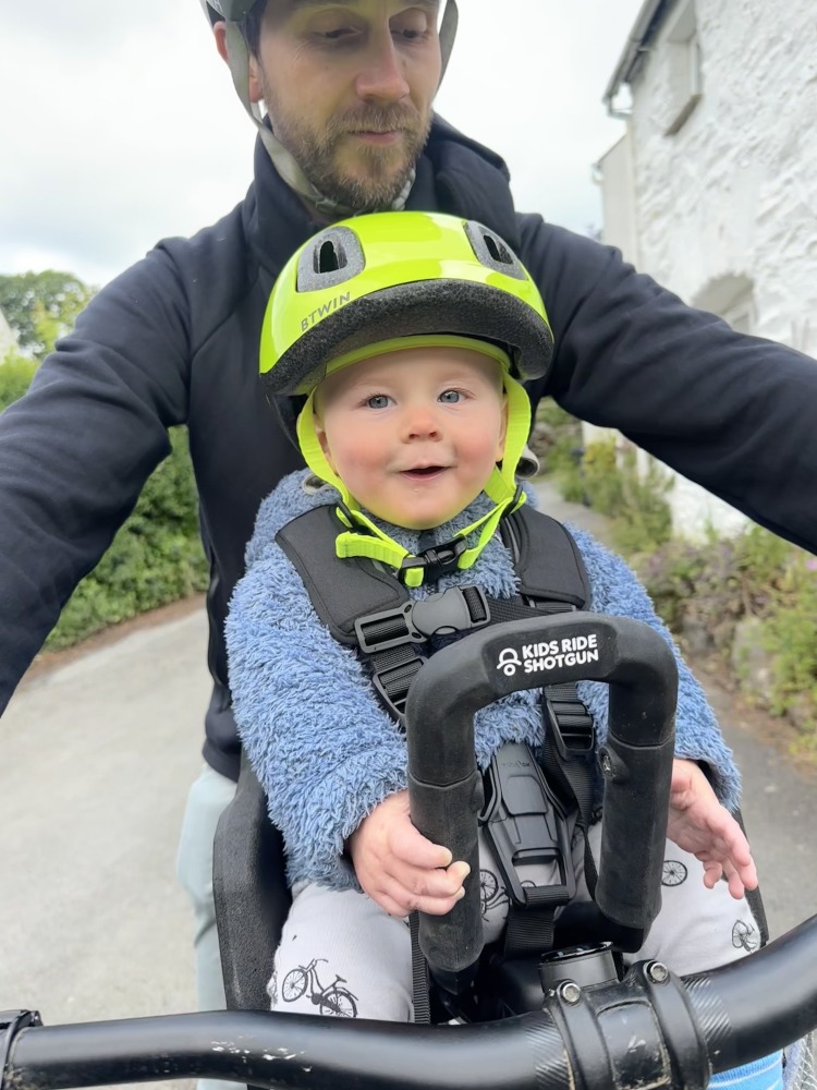 A little boy with a yellow helmet and sunglasses smiling on the kids ride shotgun pro evo seat with his dad
