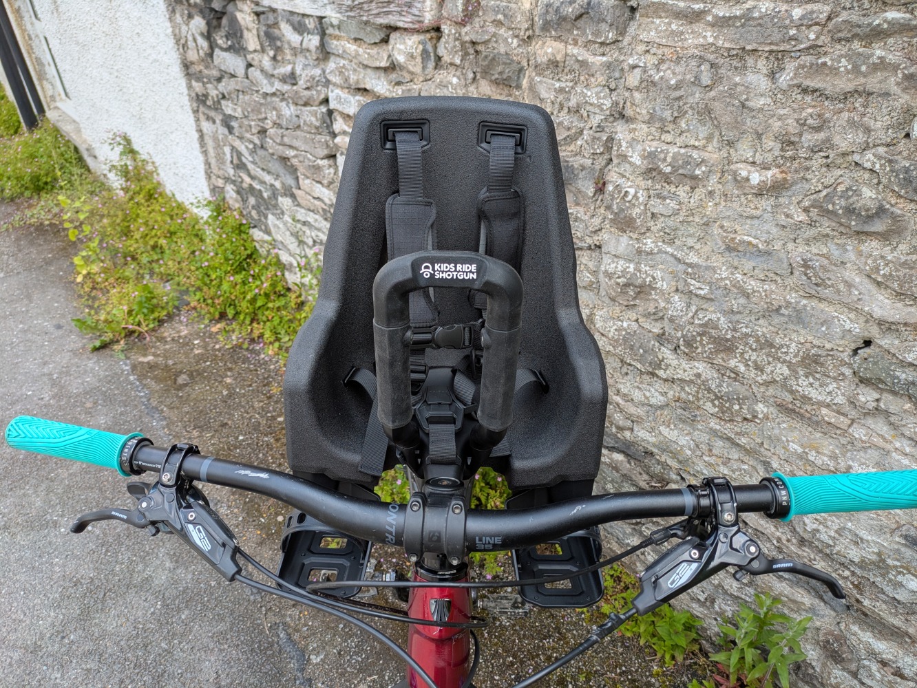 A Kids Ride Shotgun Pro Evo reat mounted to a red mountain bike leant against a stone wall