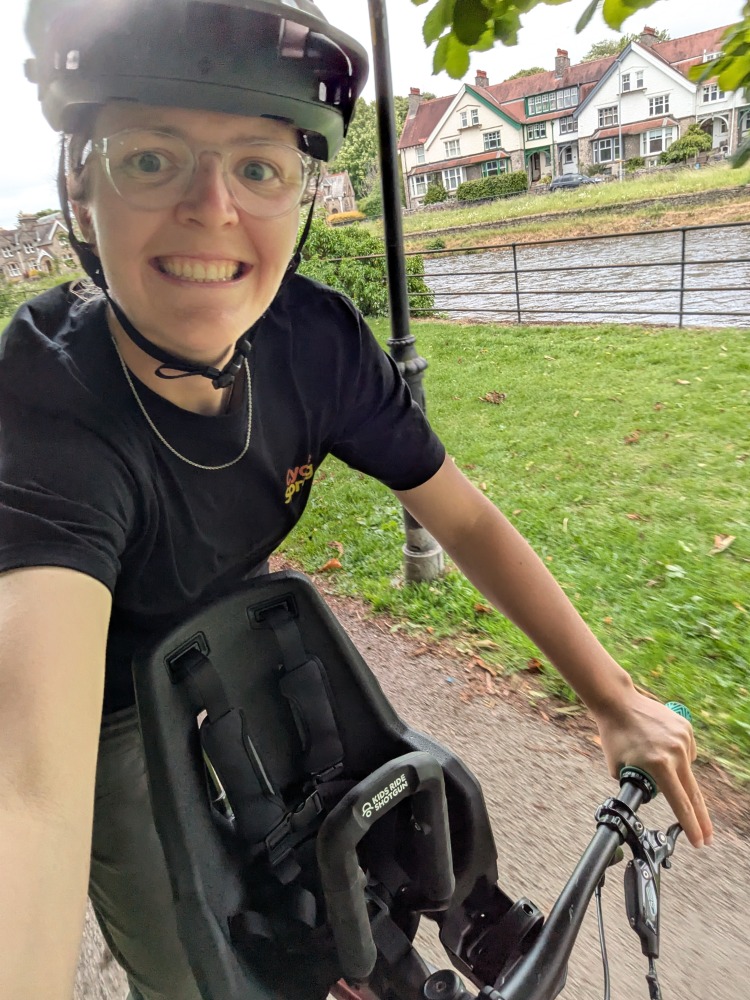 Emily, a woman in a black tshirt riding a bike with the Kids Ride Shotgun Pro Evo seat for Review