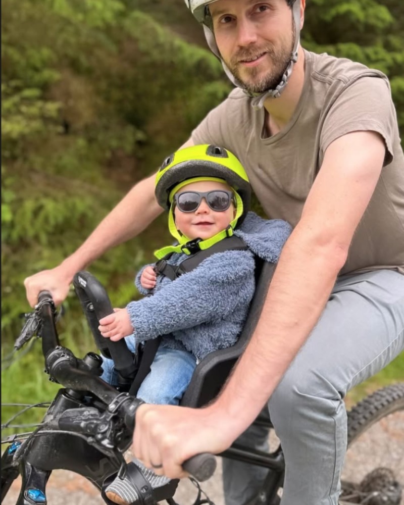 The Kids Ride Shotgun pro evo in use- a smiling baby with sunglasses on on a bike ride with his dad