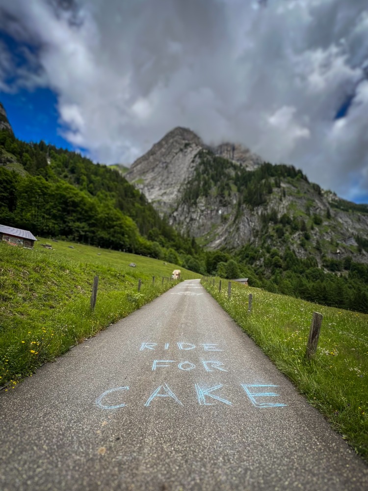 Credit Tom Kingston 20 A tarmac road leading the mountains, with 'ride for cake' written on it in chalk