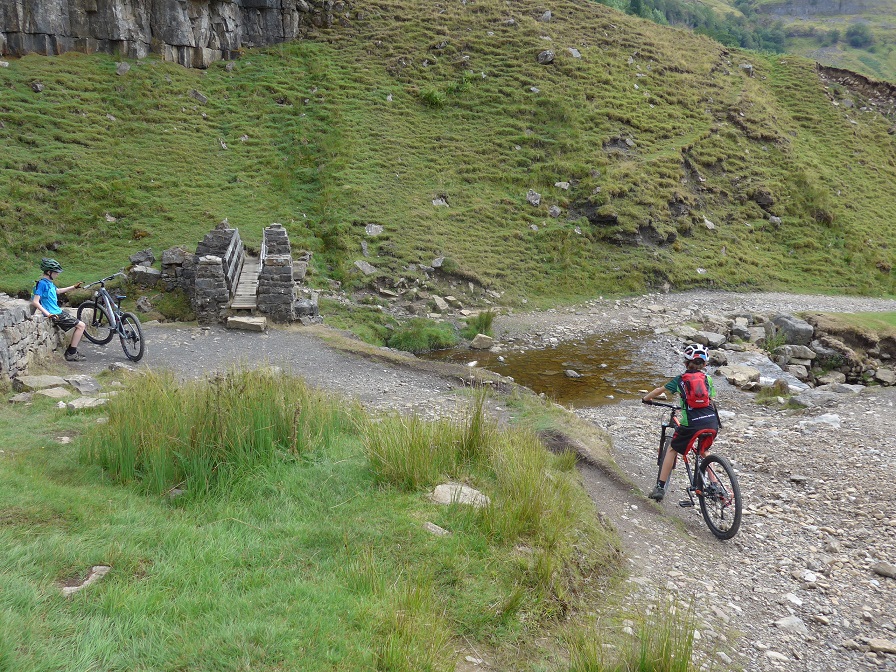 Crossing the ford on Swale Trail A couple of boys on their mountain bikes traversing a rocky track leading to a small bridge