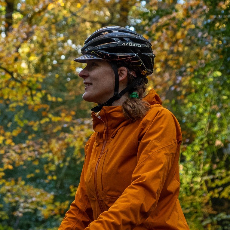 Gravel Guide_Landscape Extra–2 Hetty Kingston seen from the side, wearing a waterproof jacket and bike helmet, with trees behind her