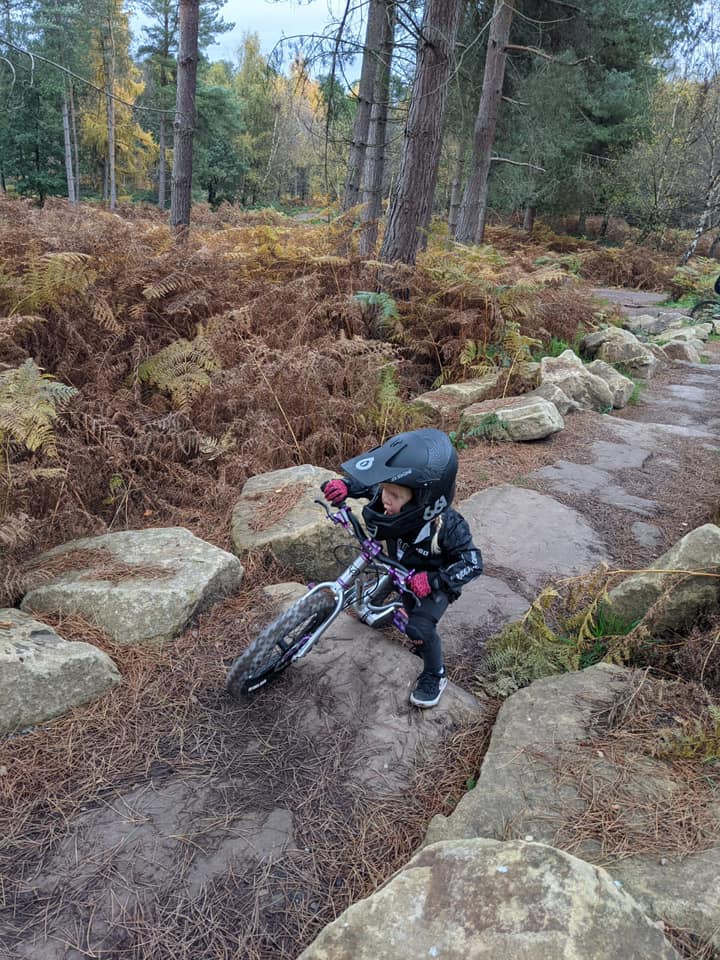 Laura Rees – Cannock A little girl in a full face helmet wheeling her mountain bike over some large rocks
