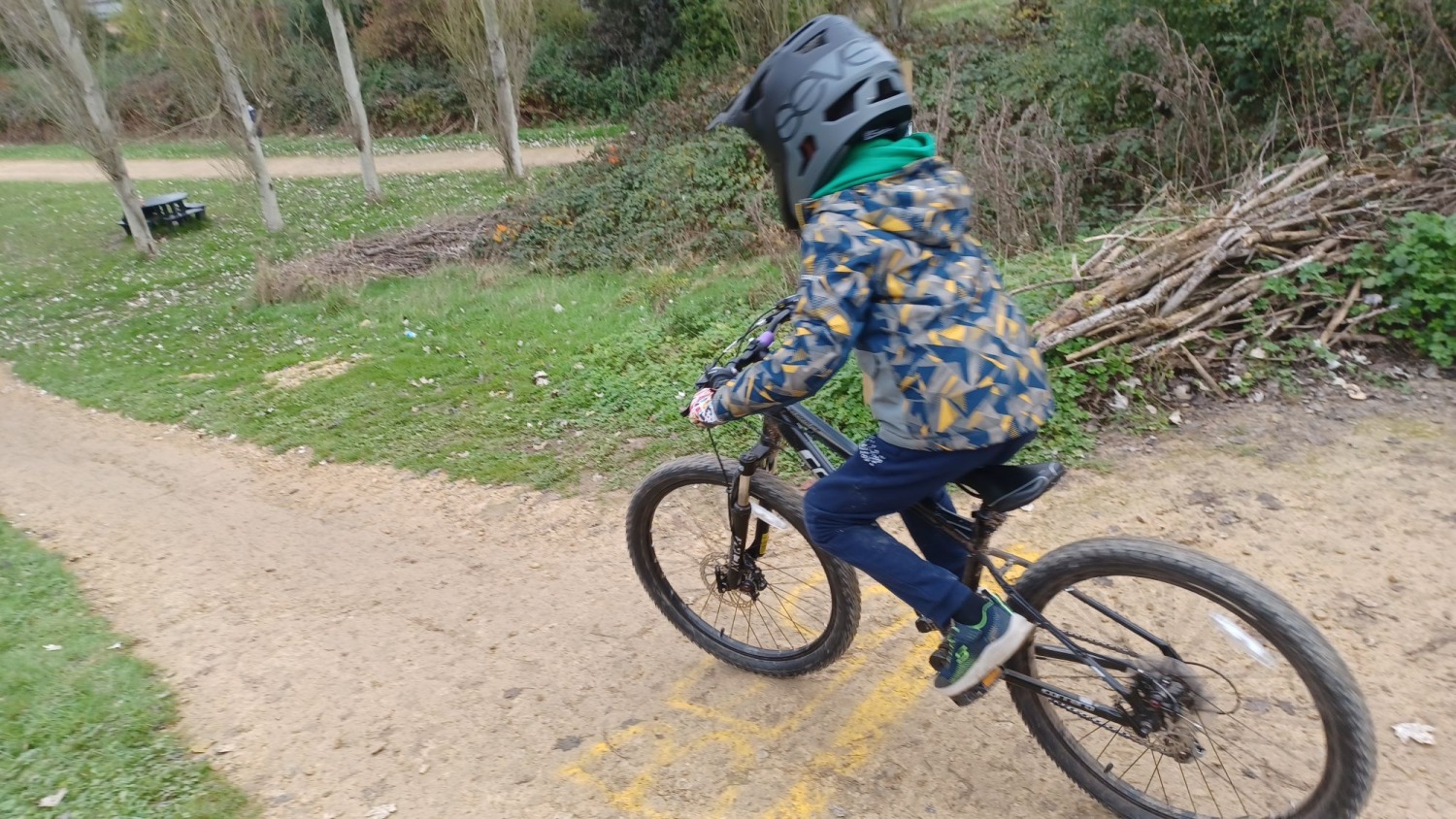 Ruth Preece – Northampton bike park A child on a mountain bike with a full face helmet, riding down a dirt track, seen from behind