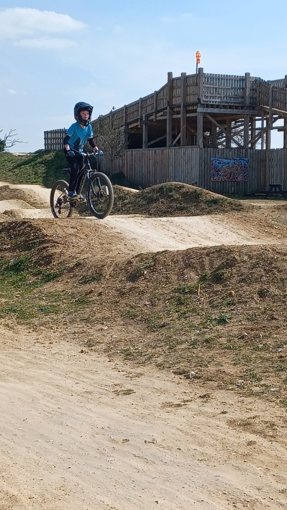 Ruth Preece – Phoenix A child wearing a full face helmet, riding their mountain bike over a gravel pump track