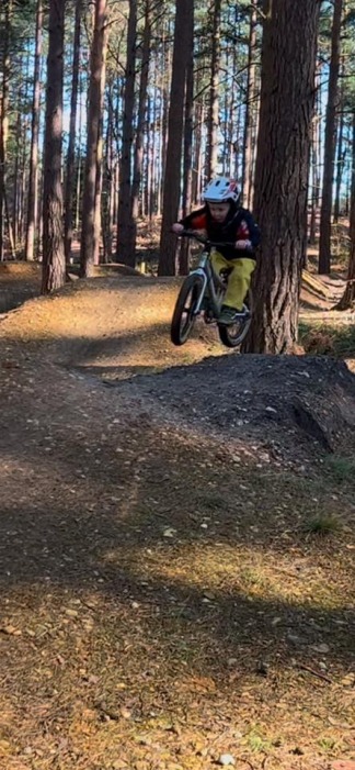 Sarah McWilliam-Free – Swinley A small child on a small pedal bike, wearing a full face helmet and pictured in mid-air while riding some jumps on a gravel pumptrack