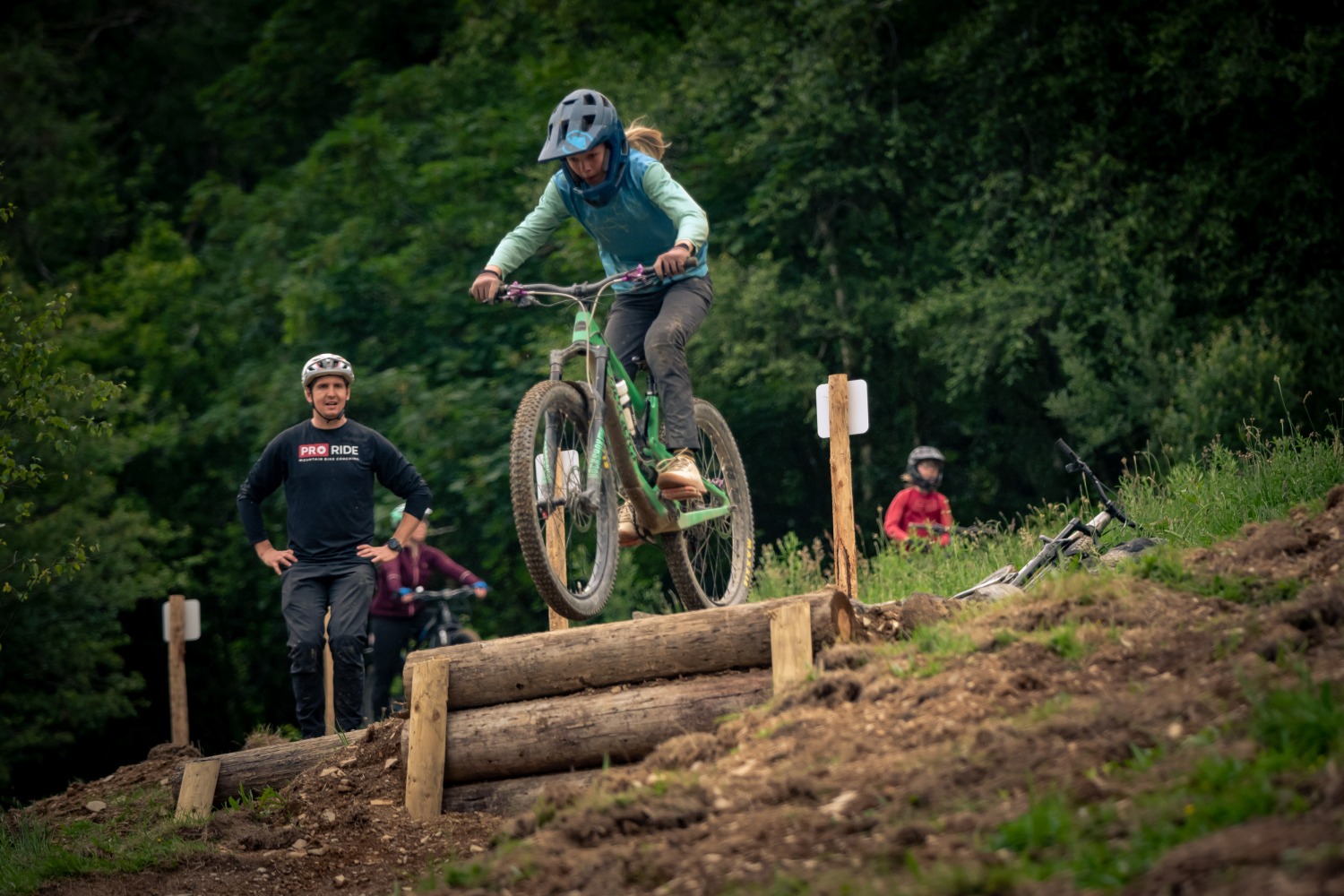 Steve Smith – Hafod A young girl wearing a full face helmet, about to ride her mountain bike over a large drop off, with a man watching in the background