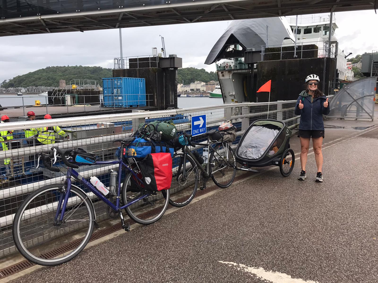 a mum smiling next to bikes and the Hamax Outback trailer waiting for a ferry in scotland