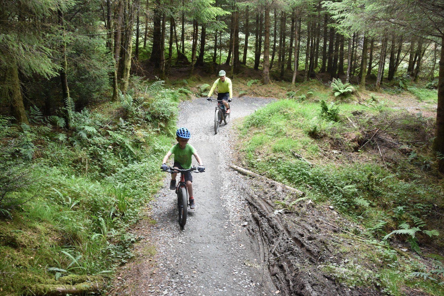 7 year old boy riding a red 20 inch BTWIN EXPL 900r mountain bike at a trail centre accompanied by an adult male