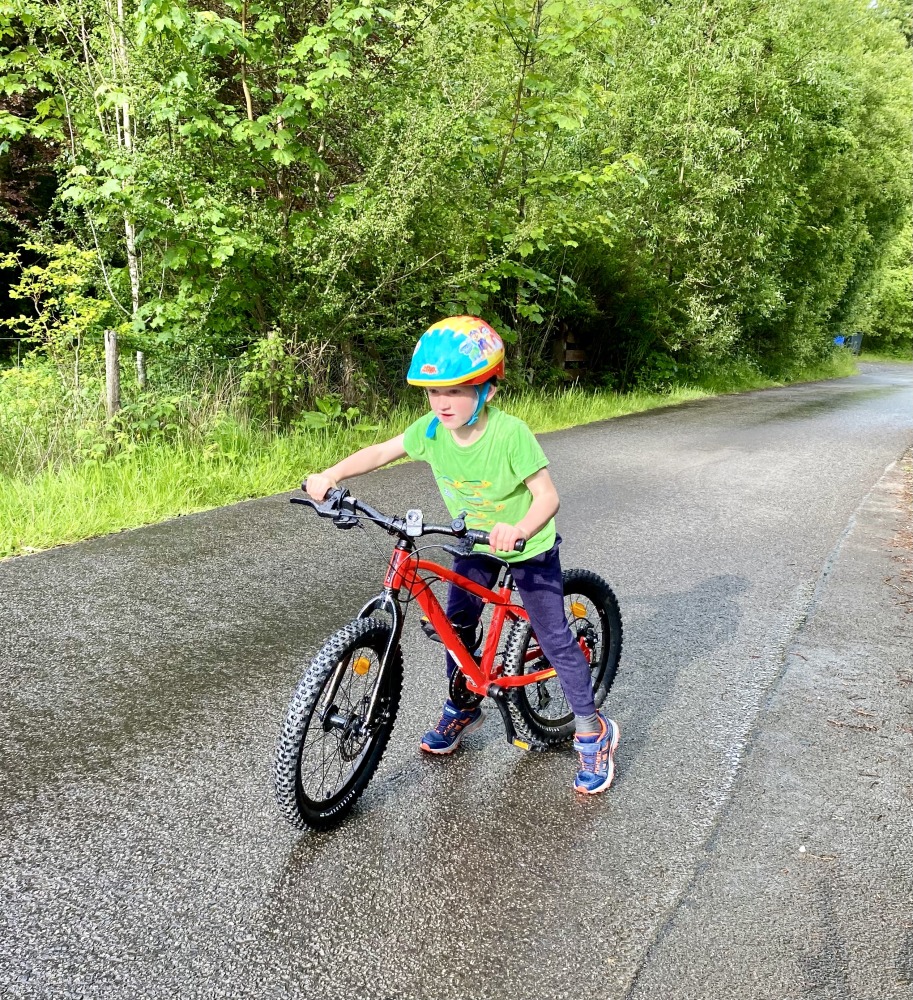 A little boy in a green top riding the Red 20 inch BTWIN EXPL 900r