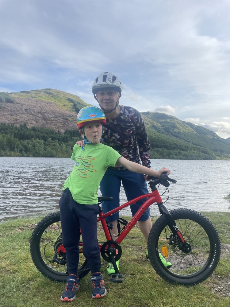A little boy in an orange top withi his mum and the Red 20 inch BTWIN EXPL 900r