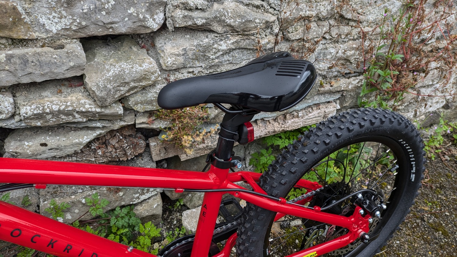 Red 20 inch BTWIN EXPL 900r leant against a wall- close up of the saddle