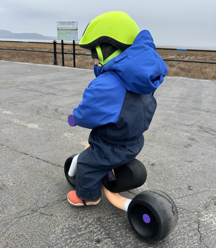 Toddler riding the woom WOW balance bike along on a smooth paved surface in Winter
