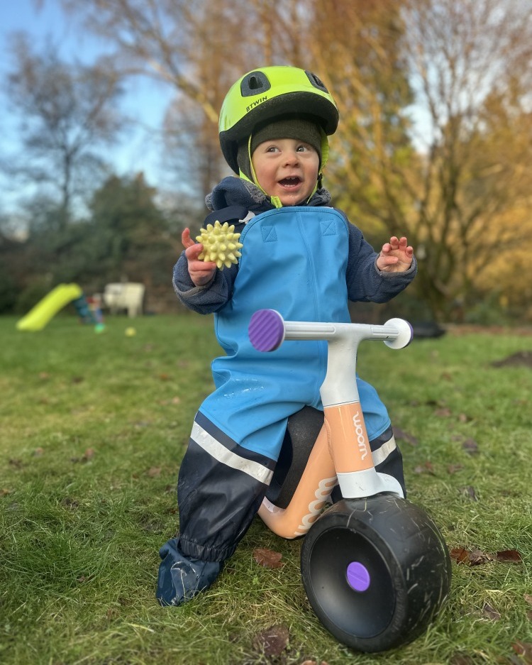 The woom wow balance bike being ridden by a toddler on grass