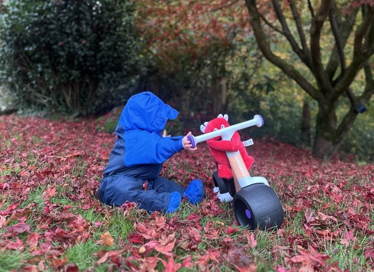 woom WOW first ride on bike - toddler sat next to the bike outside with buddy the soft toy attached to the handlebars