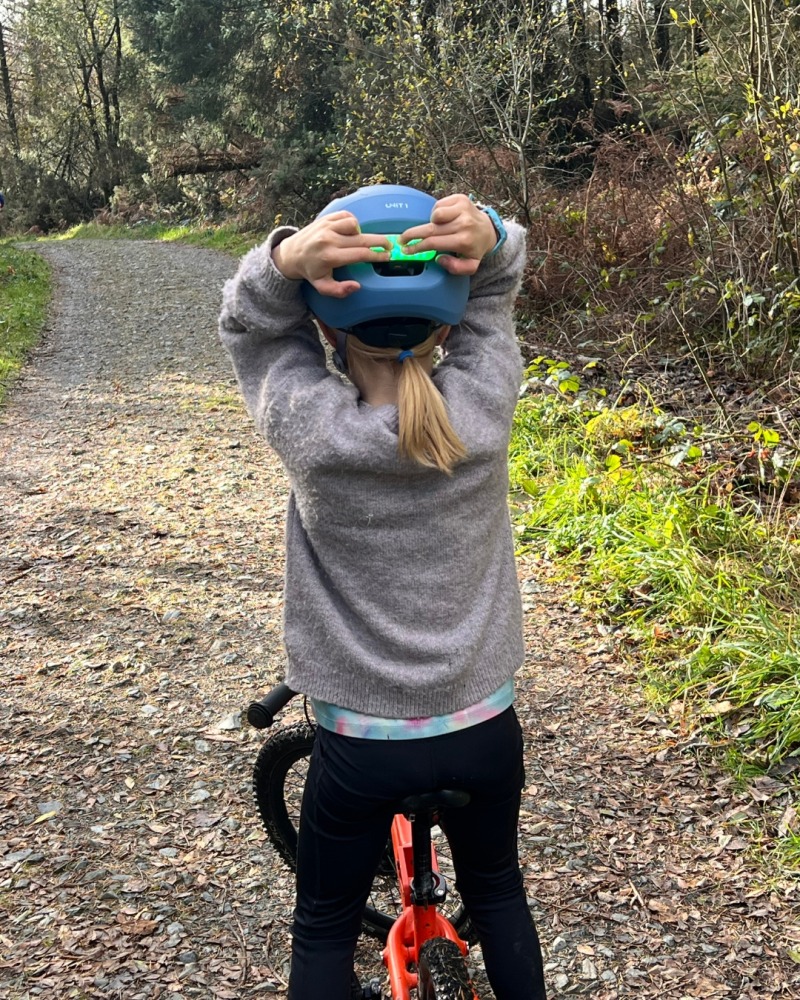 A girl wearing a blue SPARKY helmet- riding her orange mountain bike pressing the rear light