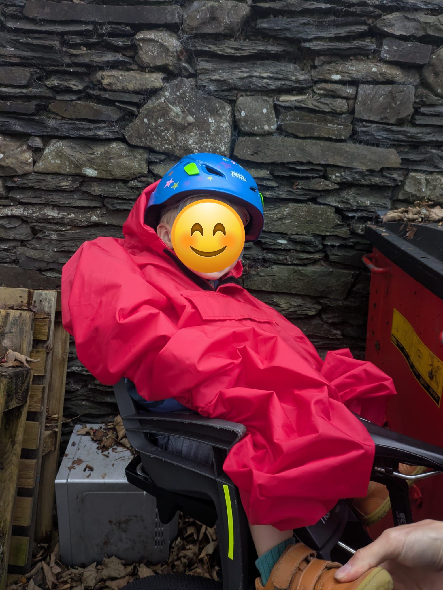 a little boy on a rear bike seat in his red Hamax Bike Seat Rain Poncho smiling