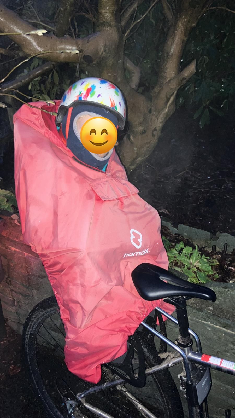 a little boy on a rear bike seat in his red Hamax Bike Seat Rain Poncho on his dads bike
