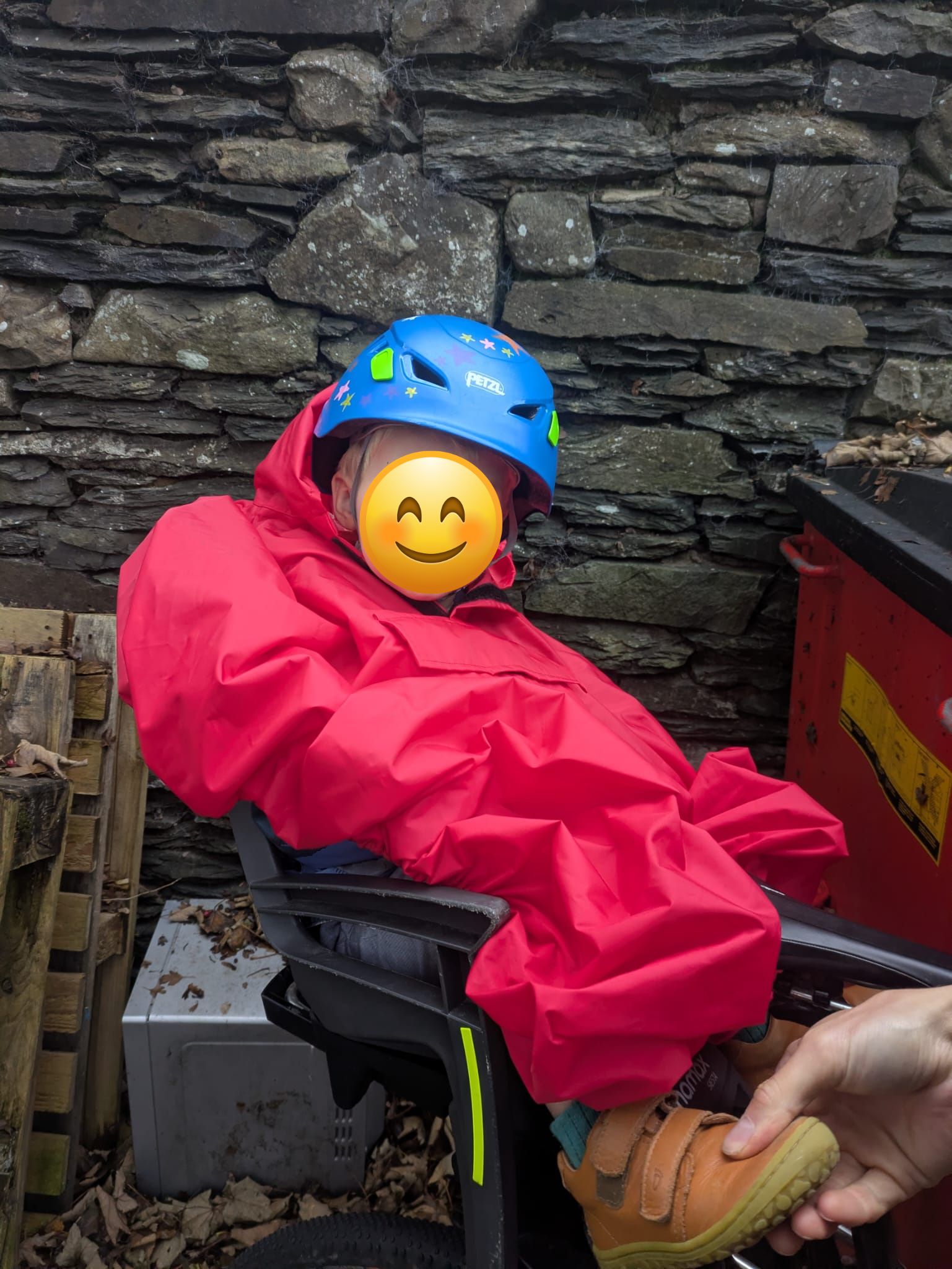 a little boy on a rear bike seat in his red Hamax Bike Seat Rain Poncho on his dads bike