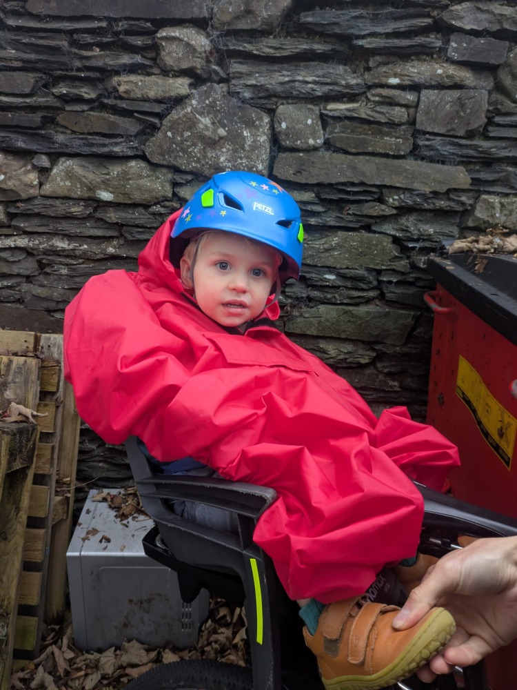 a little boy on a rear bike seat in his red Hamax Bike Seat Rain Poncho on his dads bike