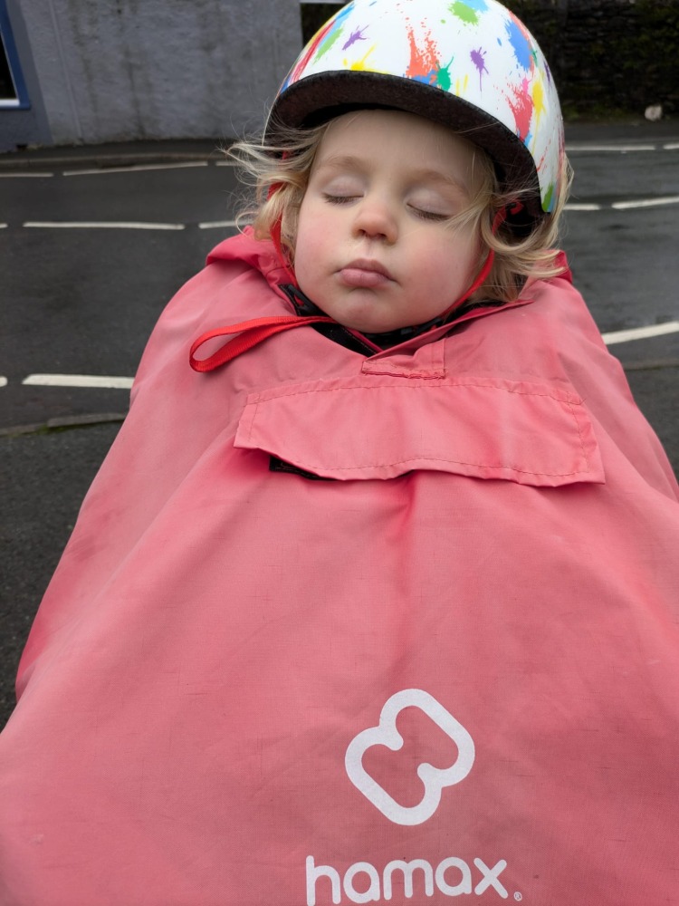 a little boy on a rear bike seat in his red Hamax Bike Seat Rain Poncho sleeping