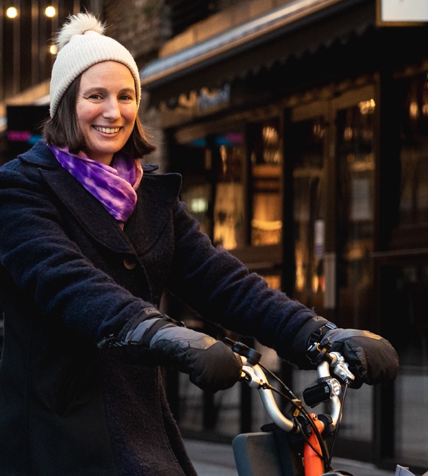 photo credit: Loud Mobility She's Electric. Photo showing woman on bicycle with white hat on, smiling at camera.