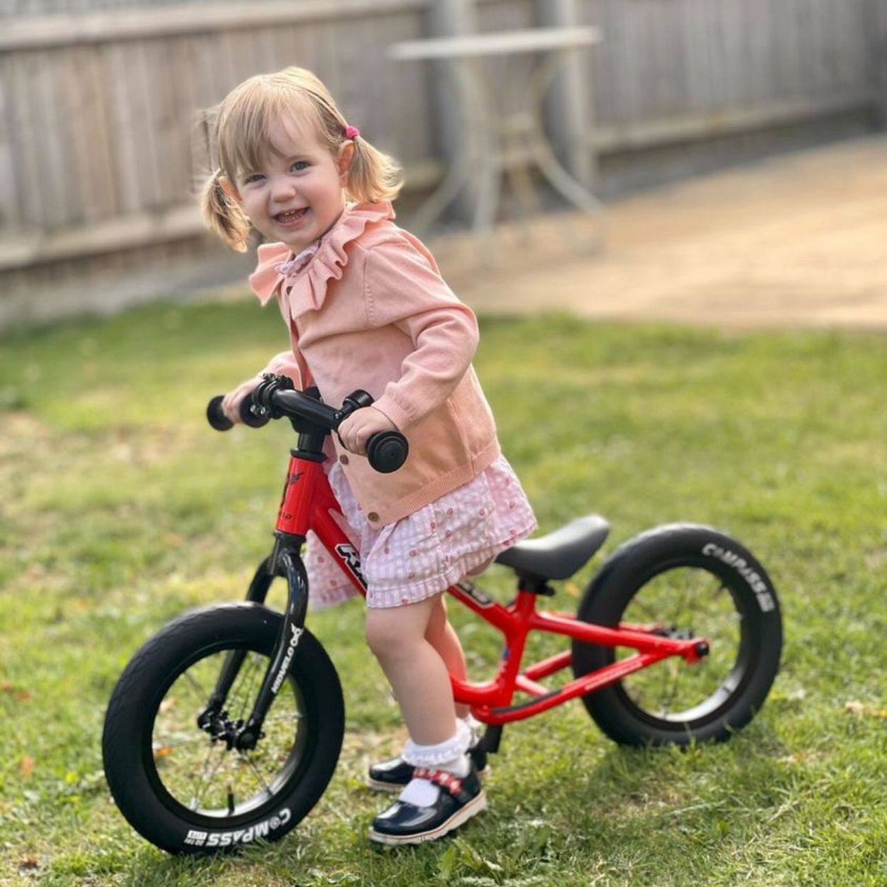 Kidvelo Rookie 12 balance bike being ridden by a 2 year old girl in a pink dress