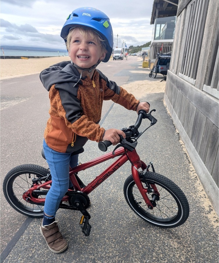 Hornit HERO 14 red kids bike being ridden by a young boy by the beach